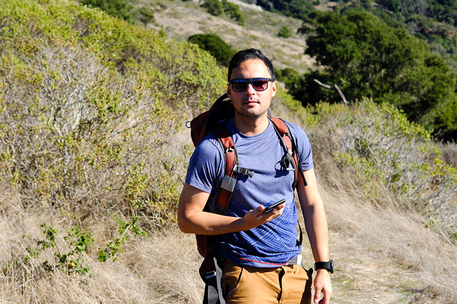 Brian hiking a brushy hillside trail with a backpack and sunglasses