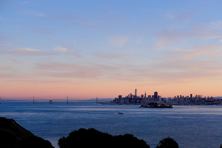 San Francisco skyline and Bay Bridge at sunset across the water