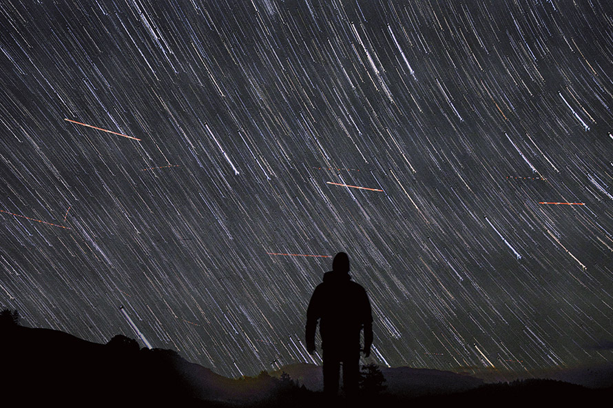 Silhouette of a person under a sky full of star trails and meteors